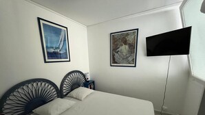 A bedroom with a bed, two wall-mounted paintings, a TV, and a nightstand. - Charming ground-floor apartment 150m from the beach  (Saint-Georges-de-Didonne)
