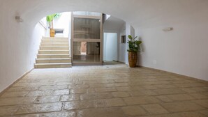 Een gang met stenen vloer, een trap die naar een kamer leidt, en potplanten.