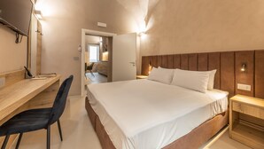Een slaapkamer met een groot bed, een houten bureau en een stoel. Er is een deur die naar een andere kamer leidt.