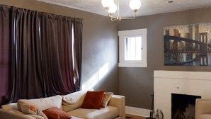Een woonkamer met een bank, een voetenbankje en een schilderij van een stadsgezicht.