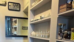 A kitchen with shelves holding jars, a clock, and a mirror.