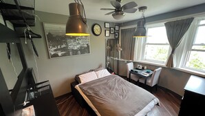 A hotel room with a bed, desk, chair, ceiling fan, and a window with curtains.