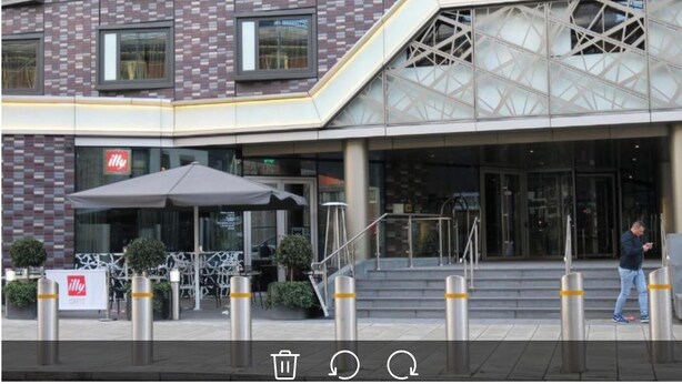 A modern building with a brick facade, a cafe named 'illy' with outdoor seating, and a staircase leading to the entrance.