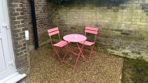 A small outdoor seating area with a round table and two chairs, surrounded by a gravel floor and a brick wall.