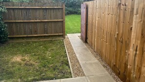 A wooden fence with a gate, a concrete pathway, and a grassy area.