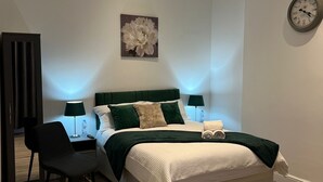 A modern bedroom with a bed, a chair, a desk, and a wall clock.