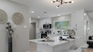 Una cocina moderna con armarios blancos, una isla central con taburetes de bar y decoración en la pared.