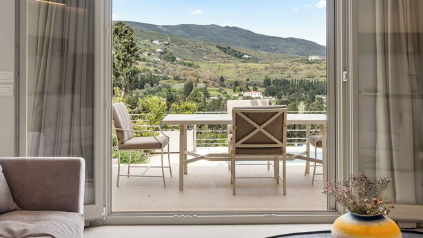 Un salon moderne avec un canapé, une table basse ronde et une vue sur un balcon agrémenté d’une table et de chaises.