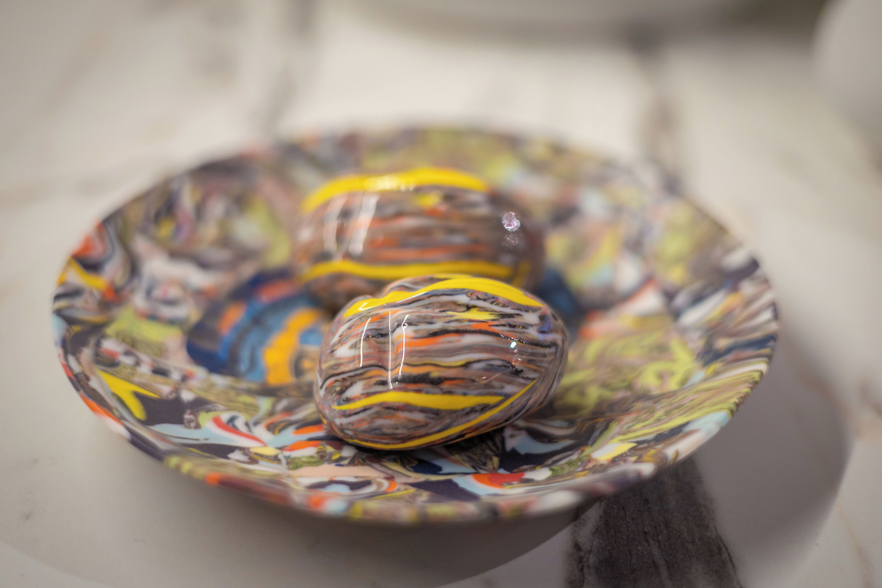Three colorful glass ornaments on a patterned plate.