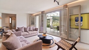Un salon moderne comprenant un canapé, un fauteuil et une table basse, ainsi que de grandes portes-fenêtres coulissantes donnant sur un balcon avec vue sur la campagne.