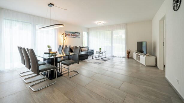 A modern living room with a dining area, featuring a sofa, chairs, a TV, and a painting on the wall.