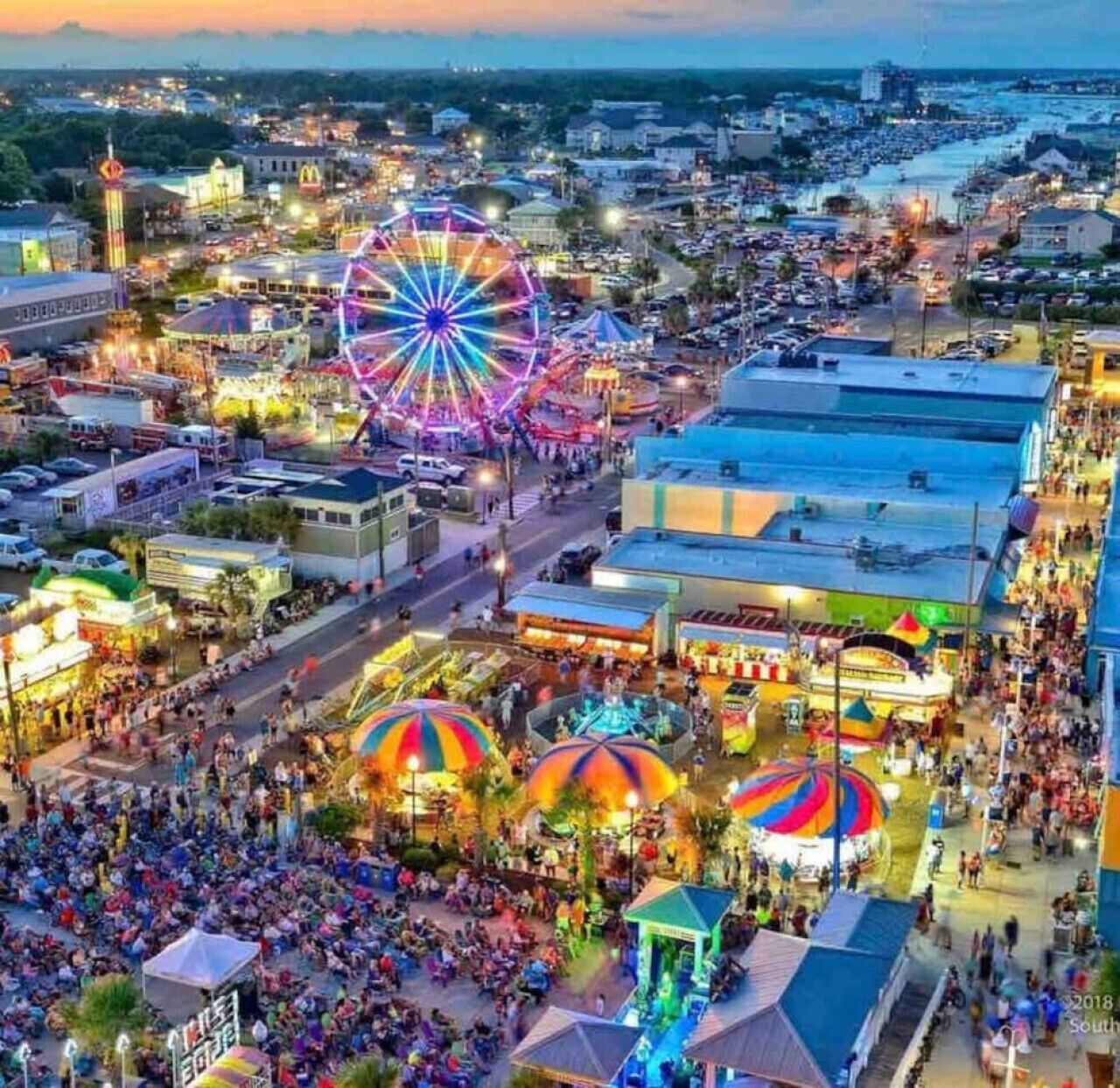 A bustling fairground with a Ferris wheel and colorful tents.