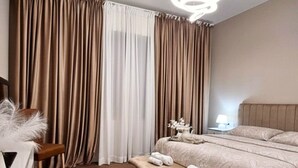 Ein Hotelzimmer mit Bett, einer Bank, einem Stuhl, einem Nachttisch mit Lampe und Vorhängen.