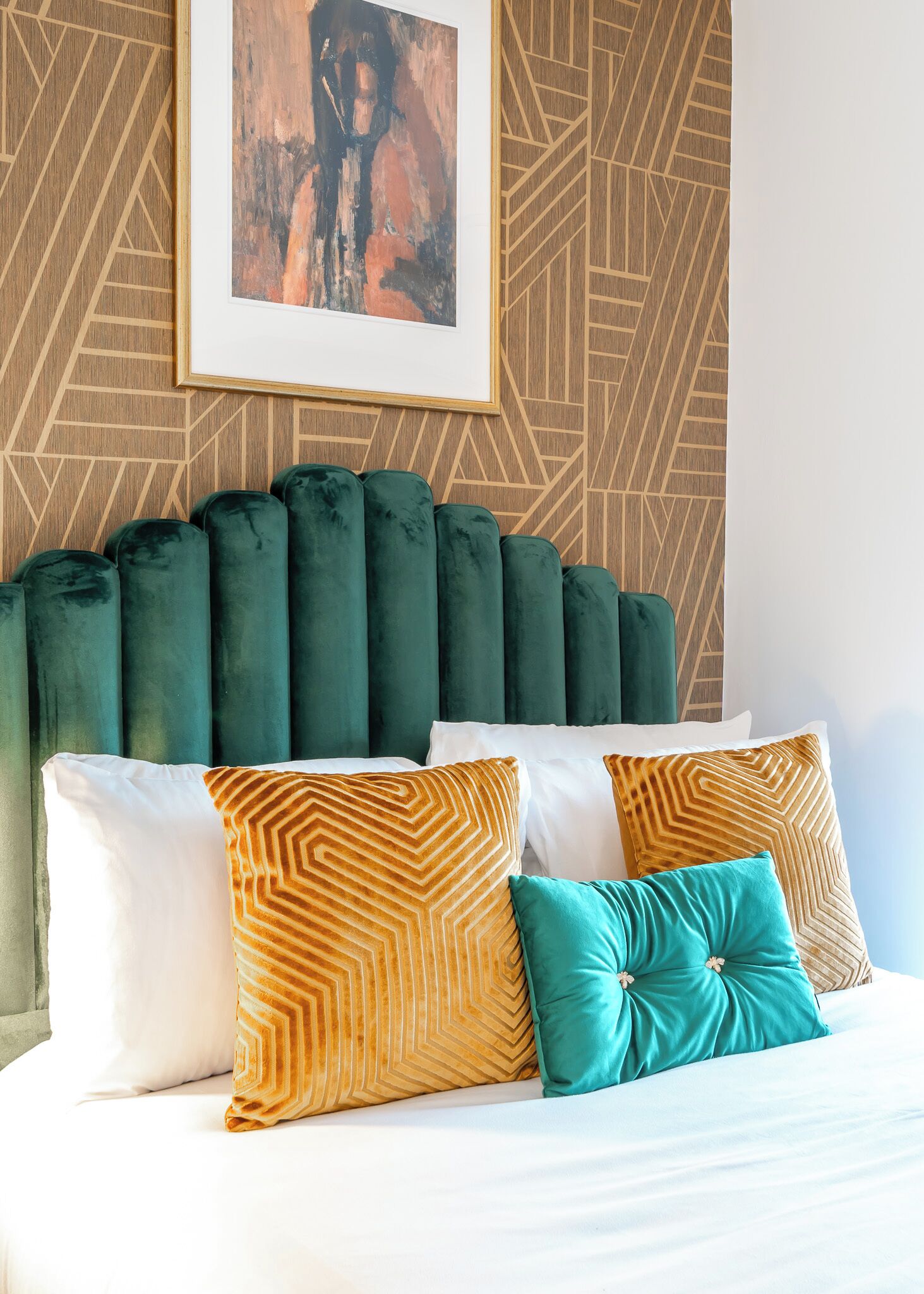 A bed with a geometric-patterned headboard, a framed abstract painting, and a variety of pillows.