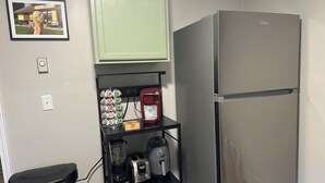 Een keuken met een koelkast, een koffiezetapparaat, een blender en een prullenbak.