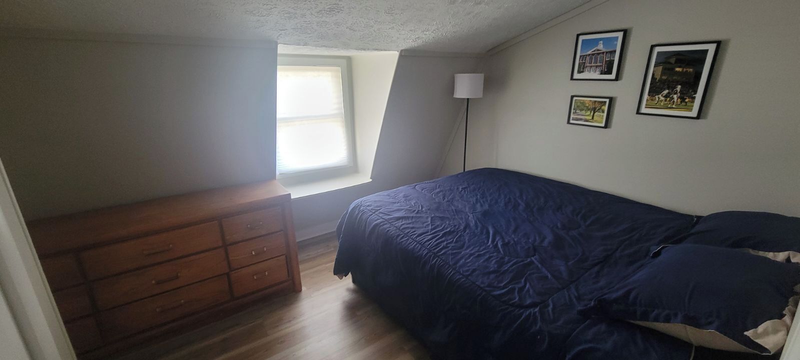 A bedroom with a bed, a dresser, a window, and framed pictures on the wall.