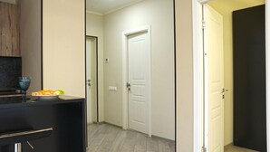 A hallway with a white door, a black door, and a closed door. There is a bowl with fruit on a counter. - 1BR Getaway w/ Pool & Sauna Access (Tsaghkadzor)