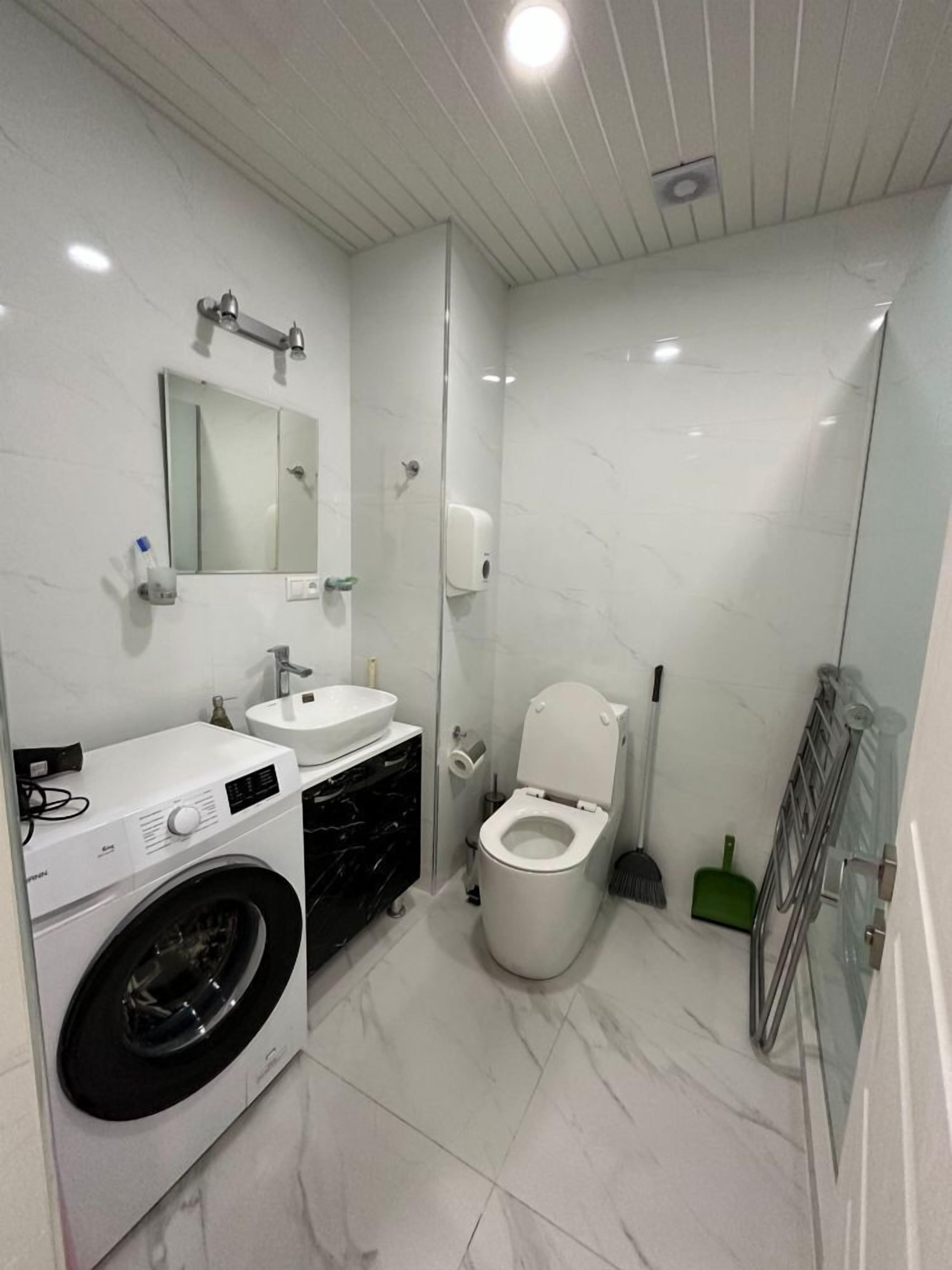Un baño pequeño con lavadora, lavamanos, inodoro y cabina de ducha de vidrio.