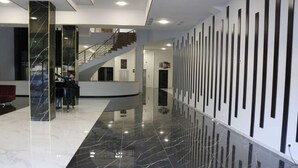 Un vestíbulo moderno con suelo de mármol pulido, una escalera y una pared decorativa con elementos verticales.
