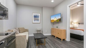 Une chambre d’hôtel compacte comprenant un coin cuisine, un canapé, une table à manger, un téléviseur et un meuble en bois.