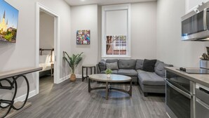 A modern kitchen with a built-in oven and microwave, a gray sectional sofa, a round coffee table, and a potted plant.