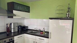 A kitchen with white cabinets, a black countertop, stainless steel appliances, and a green wall. - House directly on the beach, behind the dune, sea view (Breege)