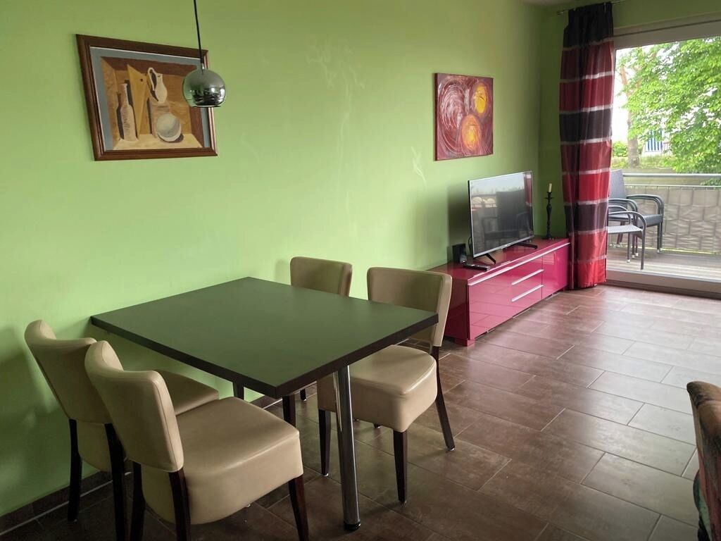 Un comedor con una mesa y sillas, un televisor sobre un mueble rojo y obras de arte en las paredes.