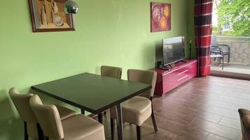 Un comedor con una mesa y sillas, un televisor sobre un mueble rojo y obras de arte en las paredes.