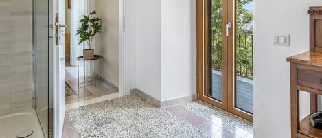 Amplia habitación con ducha, una puerta de madera que da a un balcón y un suelo con diseño.
