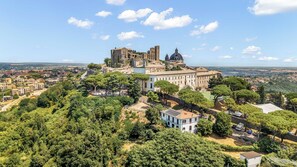 A historic building complex with multiple structures, including a prominent tower and dome, surrounded by lush greenery and a view of the cityscape. - TorripaCollection - Villa Falisca - Bolsena Lake (Montefiascone)