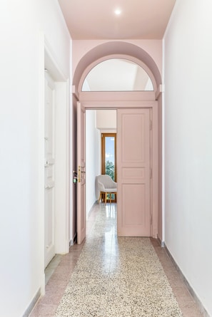 A hallway with a white door on the left, a pink door in the center, and a view of a balcony with a chair. - TorripaCollection - Villa Falisca - Bolsena Lake (Montefiascone)