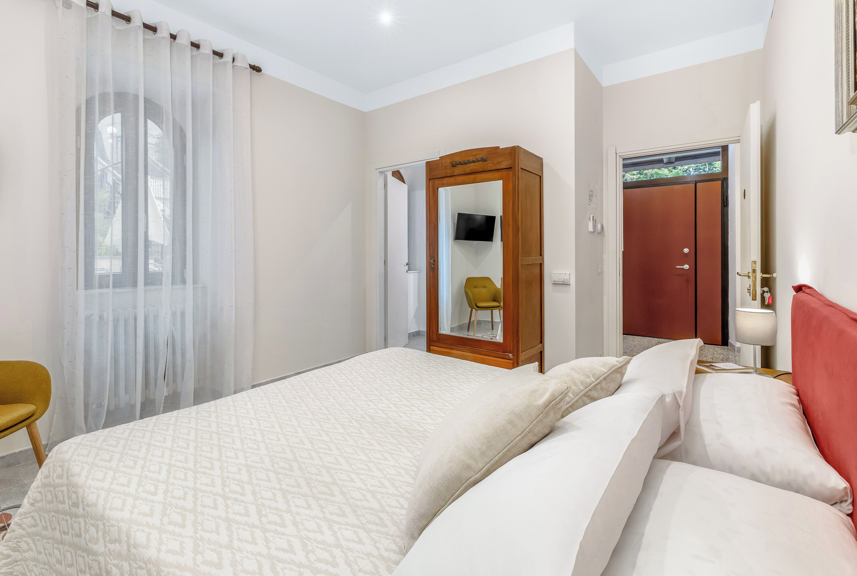 Une chambre d’hôtel comprenant un lit, une armoire, un miroir, une chaise et un bureau avec une lampe.