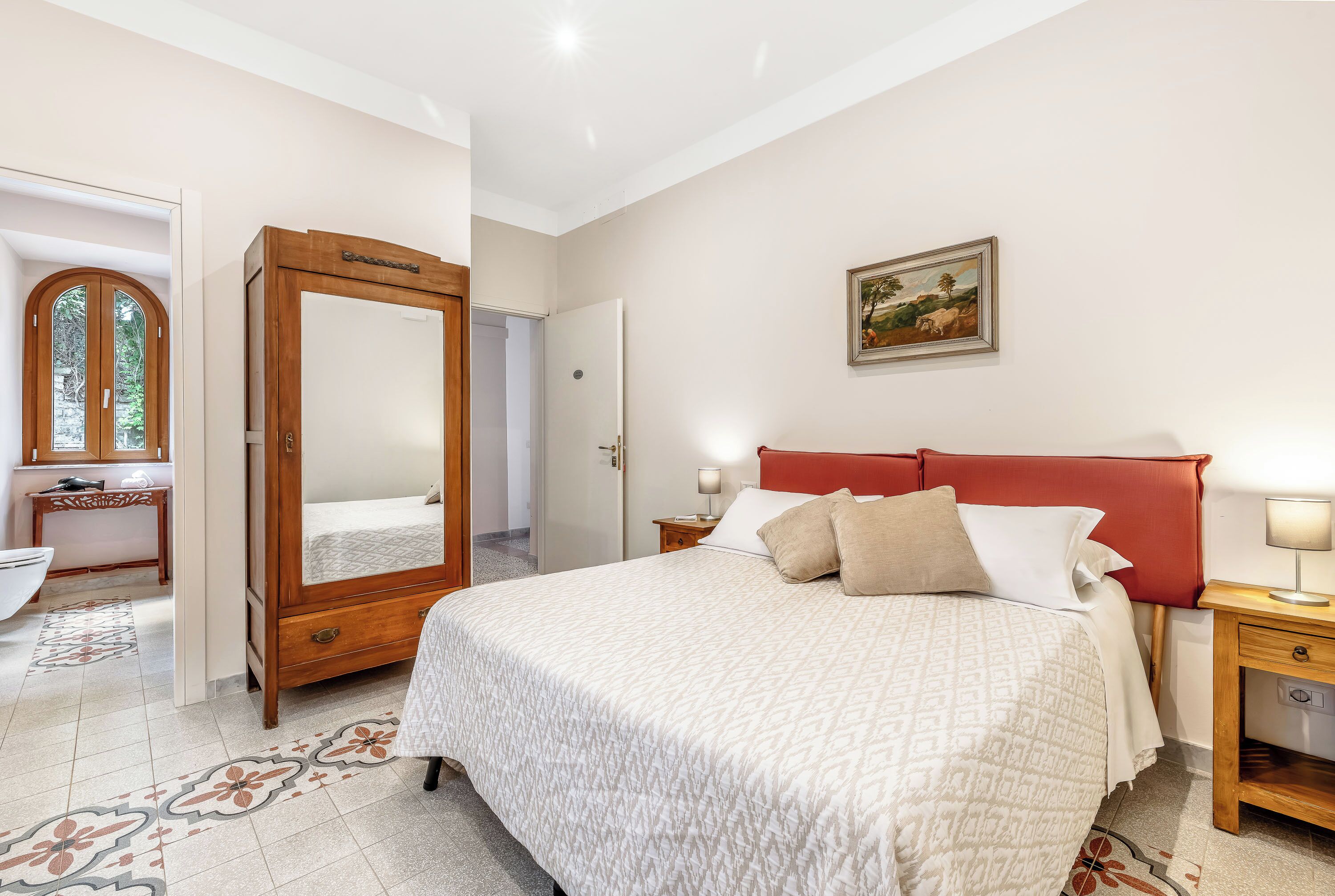 Un dormitorio con una cama grande, mesitas de noche, un armario, un espejo y un cuadro en la pared.
