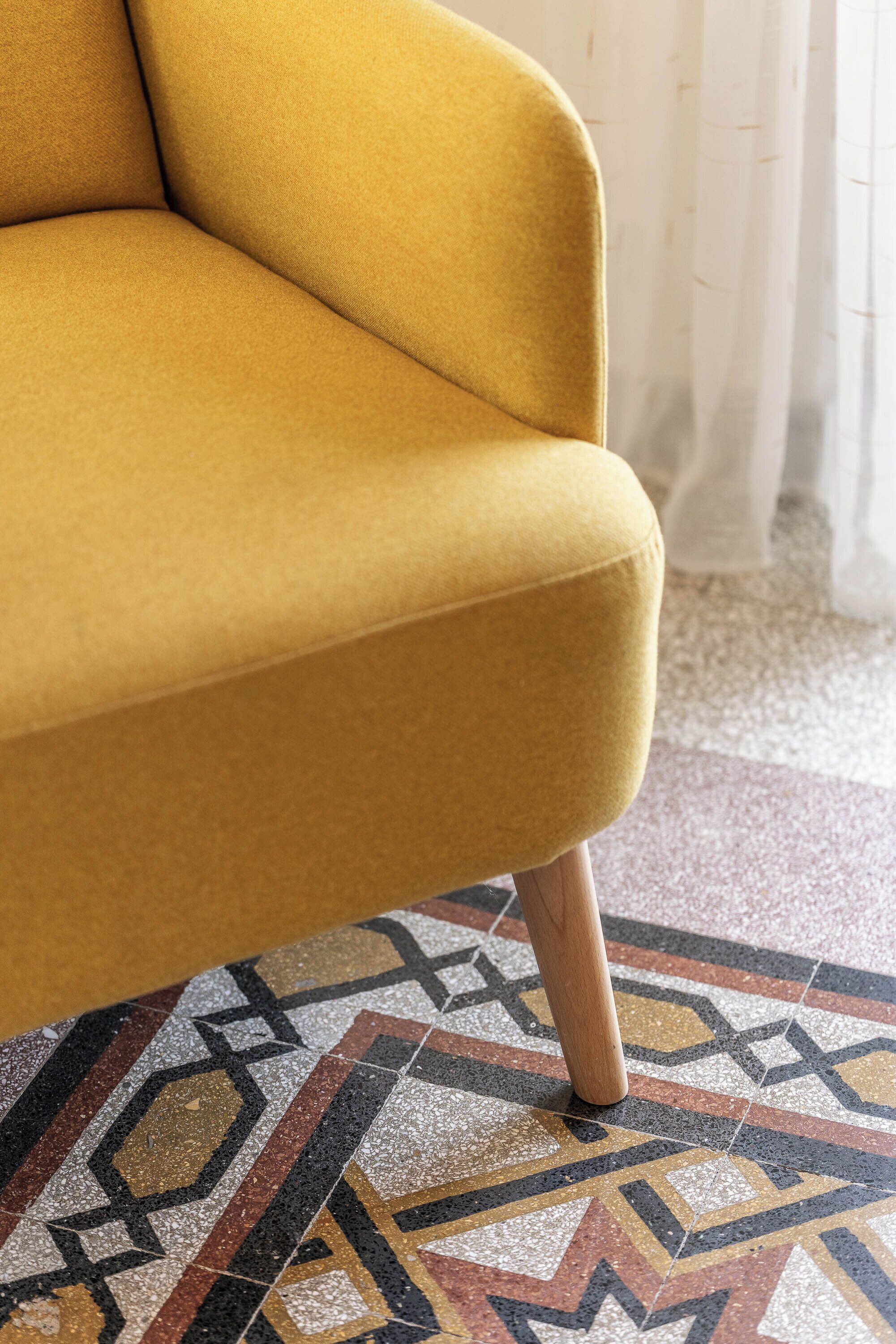 Ein gelbes Sofa mit Holzbeinen in einem Raum mit gemustertem Boden.