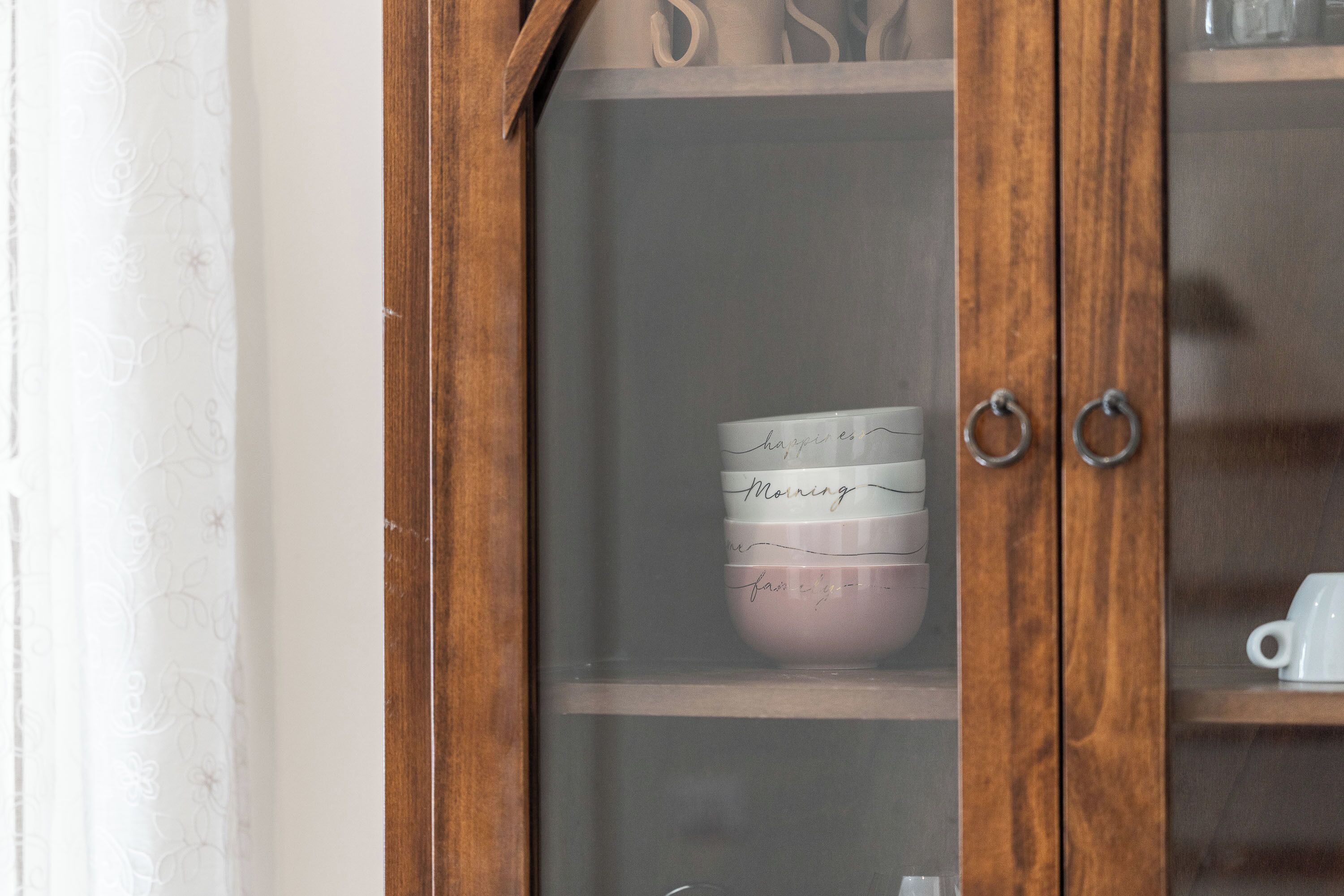 Un mueble de madera con puertas de cristal, que contiene una pila de tazas con mensajes escritos a mano.