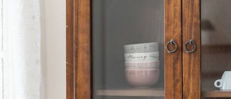 Un mueble de madera con puertas de cristal, que contiene una pila de tazas con mensajes escritos a mano.