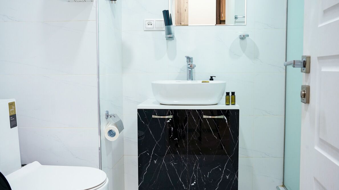Un baño con inodoro blanco, lavabo blanco y encimera de mármol negro, y cabina de ducha con paredes de vidrio.
