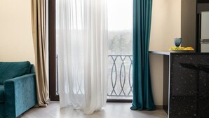 A room with a teal sofa, a kitchen counter with a bowl of fruit, and a balcony with a railing. - Cozy 1BR with Pool & Stunning Mountain Views (Tsaghkadzor)