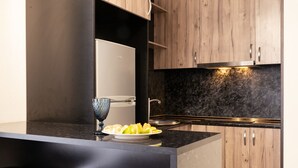 A modern kitchen with a black countertop, wooden cabinets, and a built-in oven. - Cozy 1BR with Pool & Stunning Mountain Views (Tsaghkadzor)