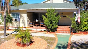 A two-story house with a covered patio, a small pool, and a flag. - Charming 2-bedroom apartment with shared Pool, frontyard WiFi, AC (St. Petersburg)