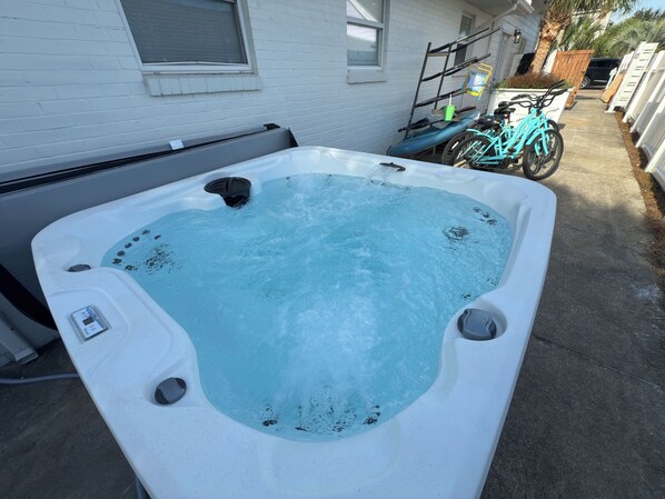 Un jacuzzi en un patio trasero con una casa blanca al fondo.
