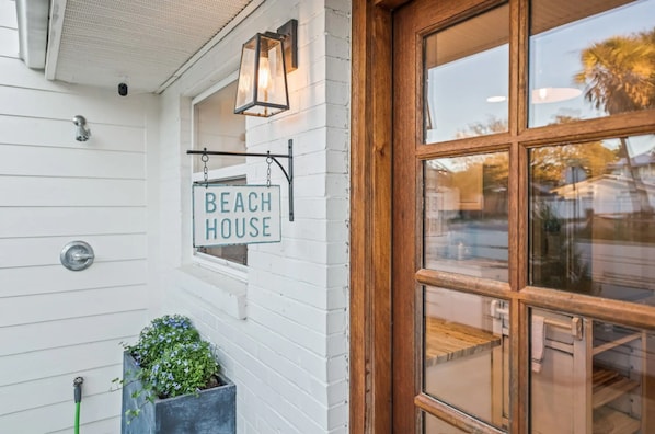 A white building with a sign reading "Beach House" and a wooden door.