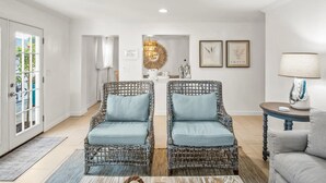 A spacious living area with wicker chairs, a round mirror, framed artwork, and a lamp on a side table. - New Golf Cart-Private Hot Tub-Walk to Beach-Charming Bungalow 4BR! (Santa Rosa Beach)