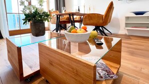Een moderne woonkamer met een salontafel met glazen blad, een schaal fruit en een bloempot.