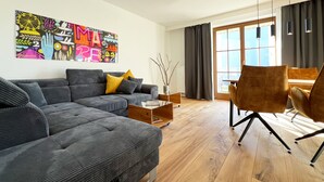 Een moderne woonkamer met een grijze bank, gele kussens, een salontafel en een groot raam met gordijnen.