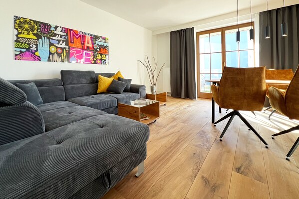 A modern living room with a grey sofa, yellow cushions, a coffee table, and a large window with curtains.