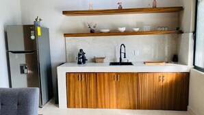 Een kleine keuken met houten kastjes, een roestvrijstalen koelkast en een klein wastafeltje.