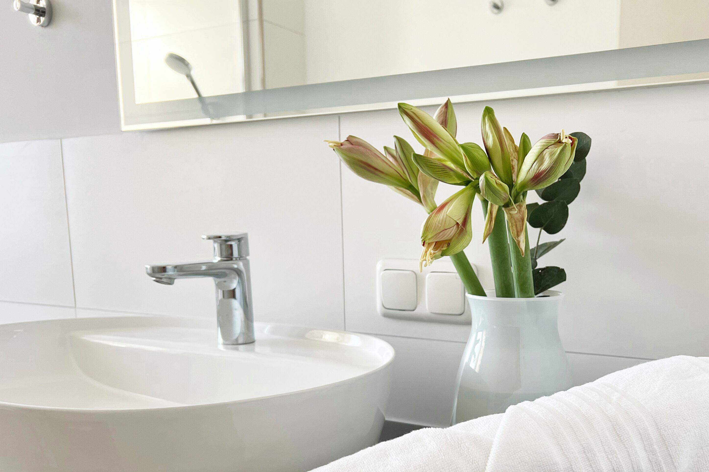 A bathroom with a white sink, a mirror, and a vase with flowers.