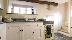 A kitchen with a central island, a stove, and a sink. - Church Cottage (Exeter)