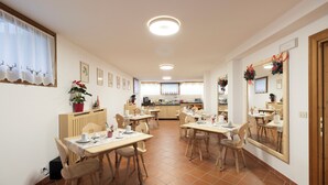 A dining area with multiple tables and chairs, a kitchen in the background, and a mirror with a festive wreath. - Chalet Stadio (Cortina d'Ampezzo)